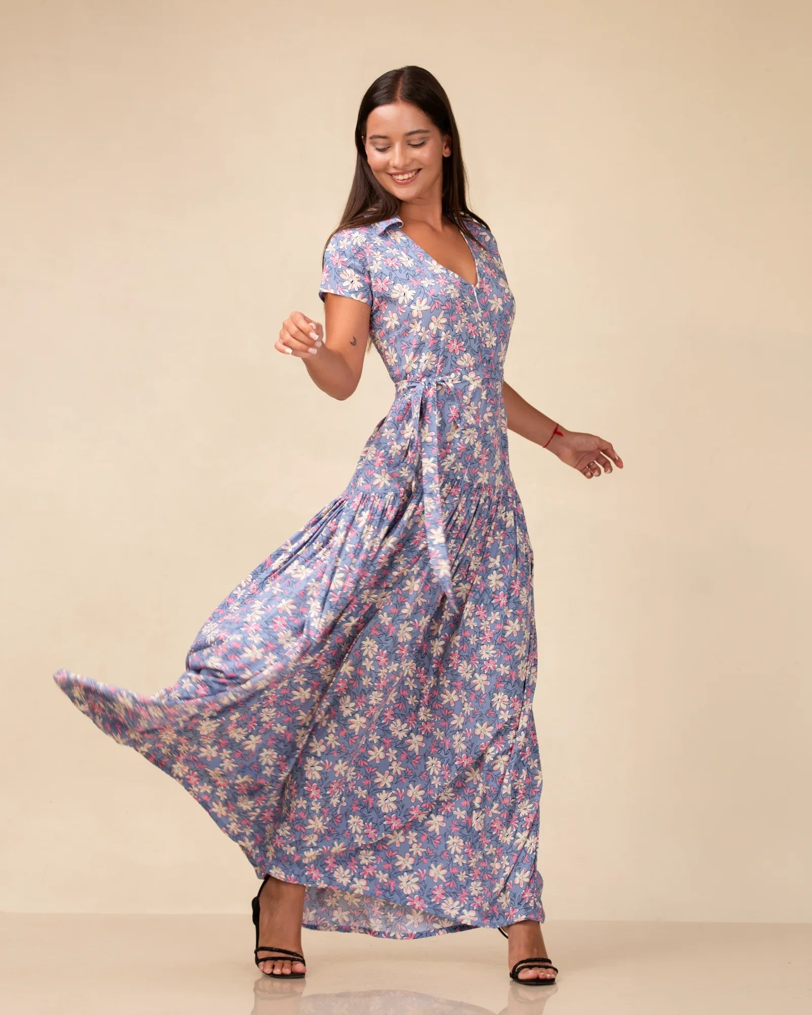 Blue floral-print collared maxi dress with cap sleeves and a tie waist, skirt caught mid-turn against a cream studio backdrop