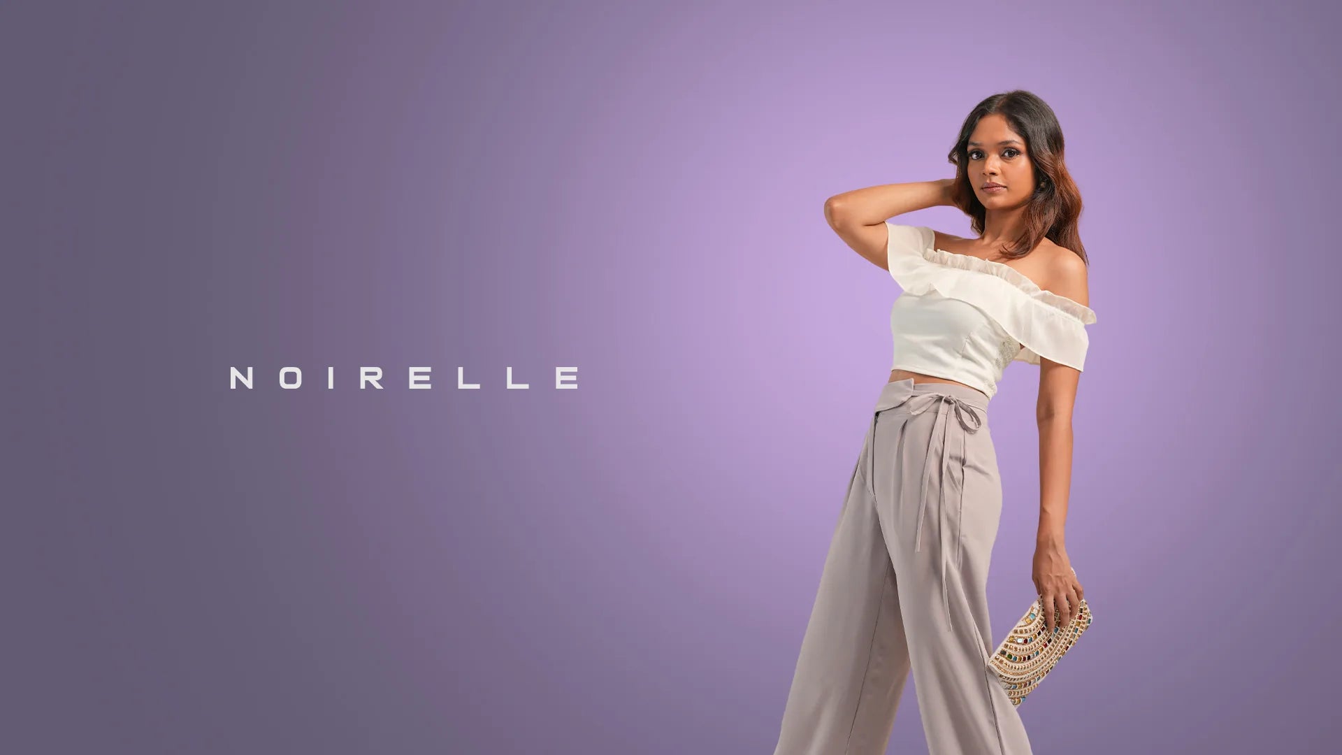 Model in an ivory off-shoulder top and taupe wide-leg trousers, Noirelle wordmark beside her on a lilac backdrop