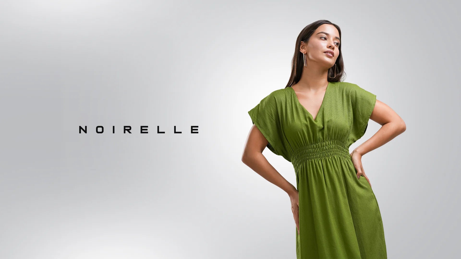 Model in an olive-green kaftan-style midi dress, Noirelle wordmark beside her on a soft grey studio backdrop